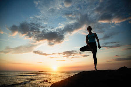 Woman doing exercises on the ocean during amazing sunset.の写真素材