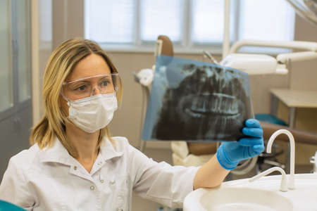Female dentist in dental office stares intently at x-ray image of jaw.