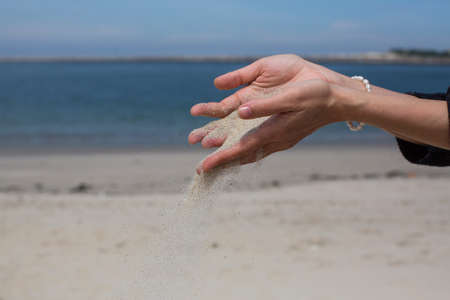 Closeup sand pours through fingers against the sea.の写真素材