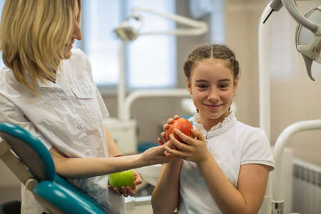 Woman dentist gives apple for smiling teenage girl in modern dental clinic.の写真素材