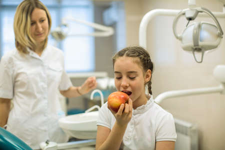 Woman dentist gives apple for smiling teenage girl in modern dental clinic.の写真素材