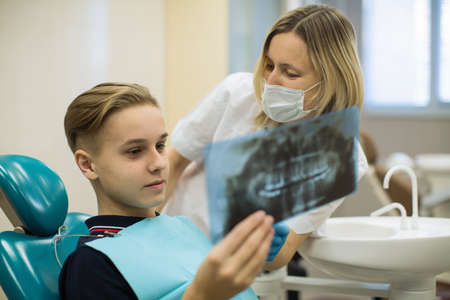 Dentist showing to young man patient x-ray the jaw at medical clinic. Stomatology medicine concept.の写真素材
