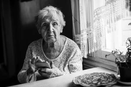 Old woman sits with a smartphone in her hands.の写真素材