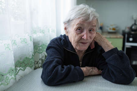 Lonely old woman sitting in the kitchen by the window in his house.の写真素材
