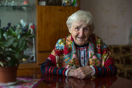 An elderly woman in bright clothes sitting at the table.の写真素材