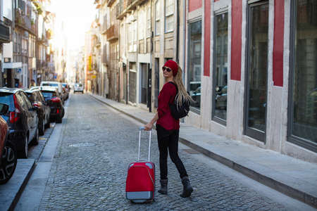 Traveler woman walking in old european town with red suitcase.の写真素材