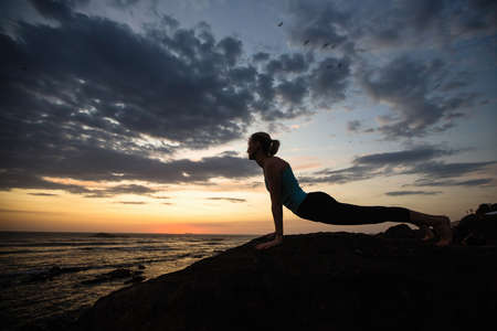 Yoga woman doing exercises on the ocean coast at twilight. Portugal.の写真素材