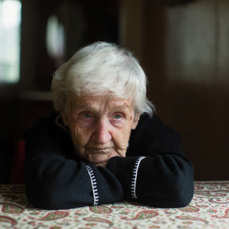Portrait of a unhappy old woman pensioner sitting at a table.の写真素材