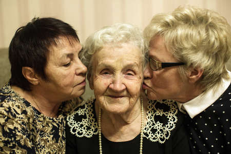 An old woman with two adult daughters sitting and hugging on a sofa.の写真素材