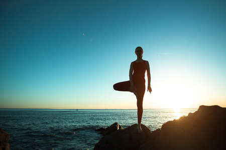 Yoga silhouette young woman doing fitness exercises on the beach at sunset.の写真素材