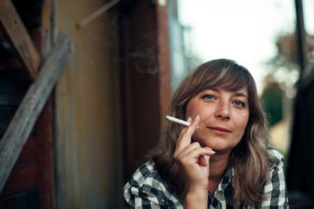 A woman smokes a cigarette sitting on the porch of a village house.の写真素材