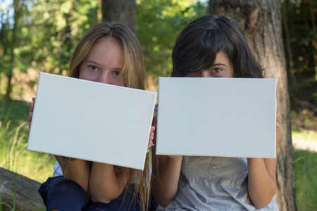 Banners for your message. Two young girl holding clean white sheet paper outdoor.の写真素材