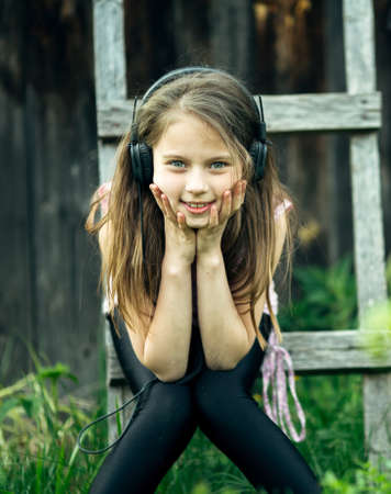 Cute little girl with headphones in the village outdoors.の写真素材
