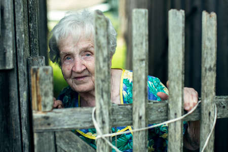 Old woman standing in the village near the fence.の写真素材