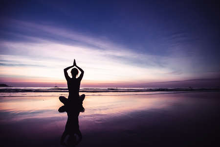 Silhouette of yoga woman in lotus position on the beach with reflection in water during twilight.の写真素材