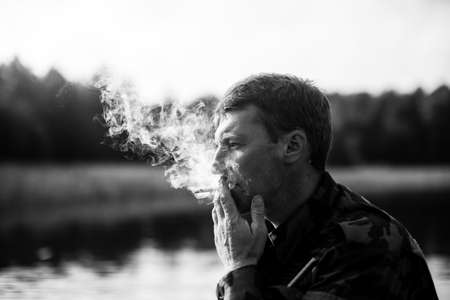 Man smoking outdoor, close-up. Smoke in the background light. Black and white photo.の写真素材