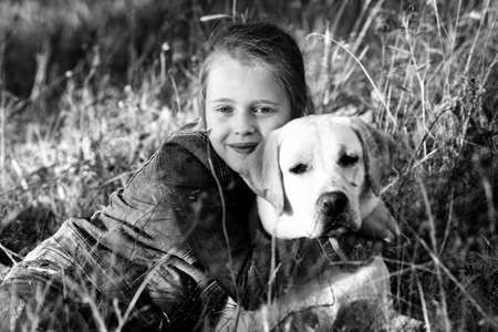 A little girl lies in the grass with the dog. Black and white photo.