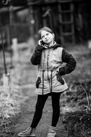 Little cute girl talking on mobile, outdoor in the village. Black and white photography.の写真素材