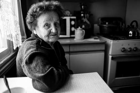 Portrait of old woman in the kitchen at rural home. Black and white photography.の写真素材