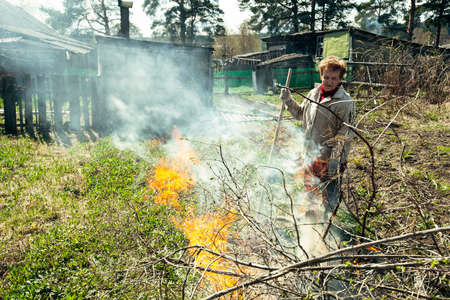 An old woman burns branches on her farm.