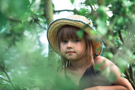 Little cute girl in a straw hat in the green park.