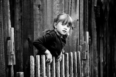 Little cute girl standing near vintage rural fence. Black and white photography.の写真素材