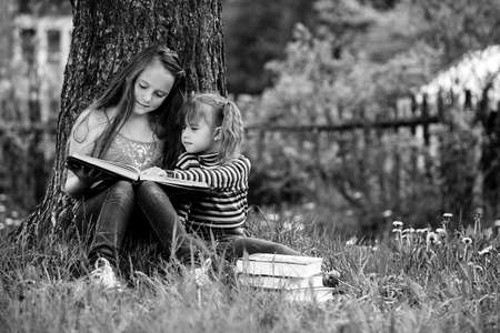 Children sisters reading the book in the summer park. Black and white photography.