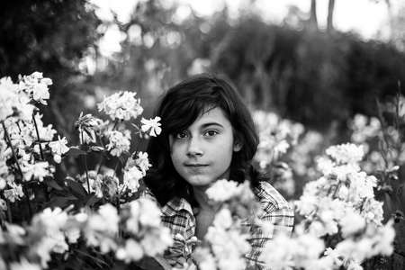 Black haired teen girl in the garden among flowers. Black and white photo.
