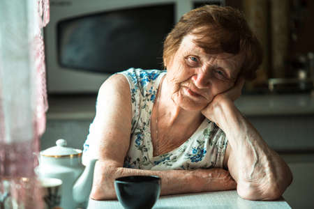 An elderly pensioner sits at a table in her home. Portrait.の写真素材