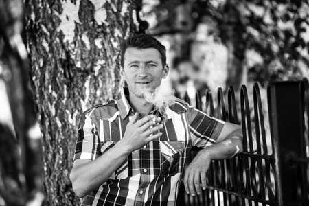 Portrait of man smoking outdoor, looking at the camera. Black and white photo.