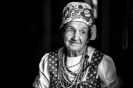 Portrait of elderly woman in ethnic clothes in her house. Black and white photo.