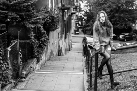 Young long-haired girl sitting on the parapet in the old town. Black and white photo.