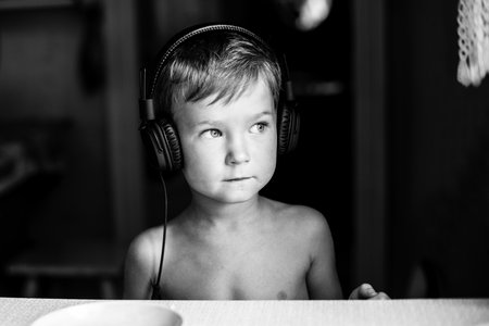 Portrait of little boy with headphones at the table at home. Black and white photo.の写真素材