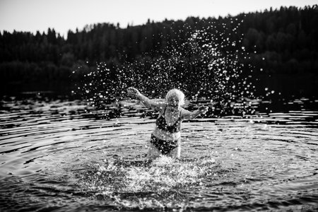 An elderly woman swimming in the summer river at sunset. Black and white photo.の写真素材