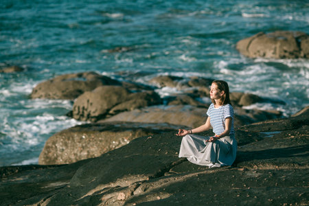 Young yoga woman meditates in the lotus position sitting on rocks on the ocean coast.の写真素材