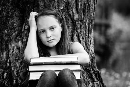 Portrait of tired teen girl with books in the park. Black and white photo.の写真素材