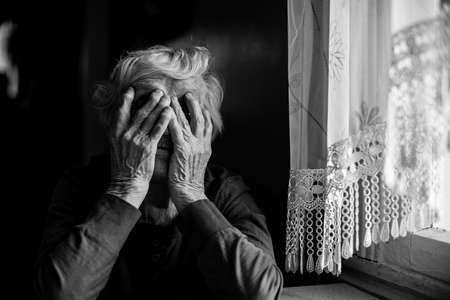 An old woman covered her face with both hands. Black and white photo.