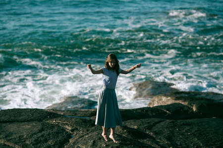 Nice young dancer woman is engaged in choreography on the rocky coast of the ocean.の写真素材