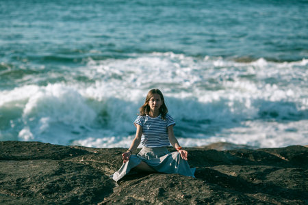 Yoga woman meditates sitting on rocks on the Alantic ocean coast.の写真素材