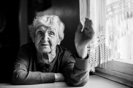 An old woman emotionally talking sitting at a table at the home. Black and white photo.の写真素材