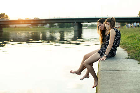 Young friend girls on the stone embankment. Beautiful soft light at sunset.の写真素材
