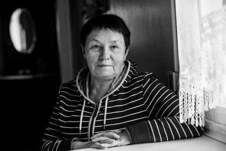 Portrait of adult woman sitting at a table in the house. Black and white photo.の写真素材