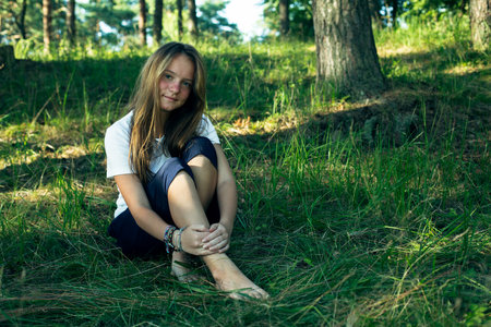 Teen girl sitting on the green grass in the park in the summer.の写真素材