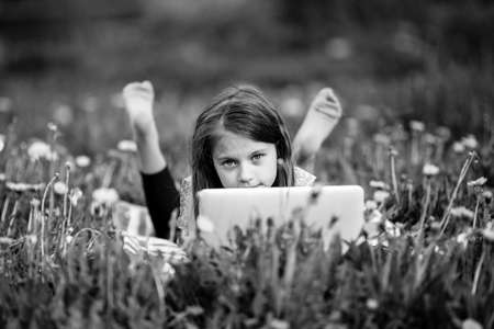 Little girl with laptop lying on outdoor at summer. Black and white photo.の写真素材