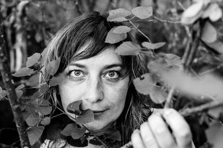 Portrait of a woman in close-up among the leaves in the park. Black and white photo.