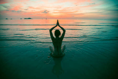 Yoga woman silhouette on the sea beach at amazing sunset. Meditation and healthy lifestyle.の写真素材