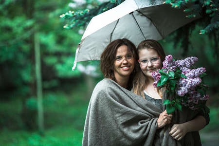 Woman under umbrella in the park with her daughter.の写真素材
