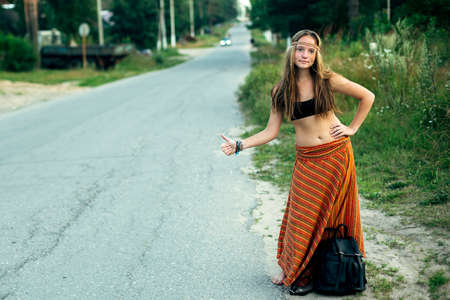 Cute girl hitchhiker votes on the highway.の写真素材