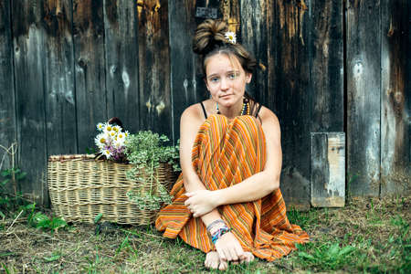 A teen girl is sitting with a basket of daisies.