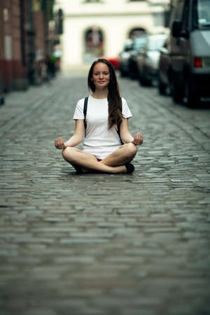 A teen girl is sitting in the lotus position in the middle of the city pavement.の写真素材